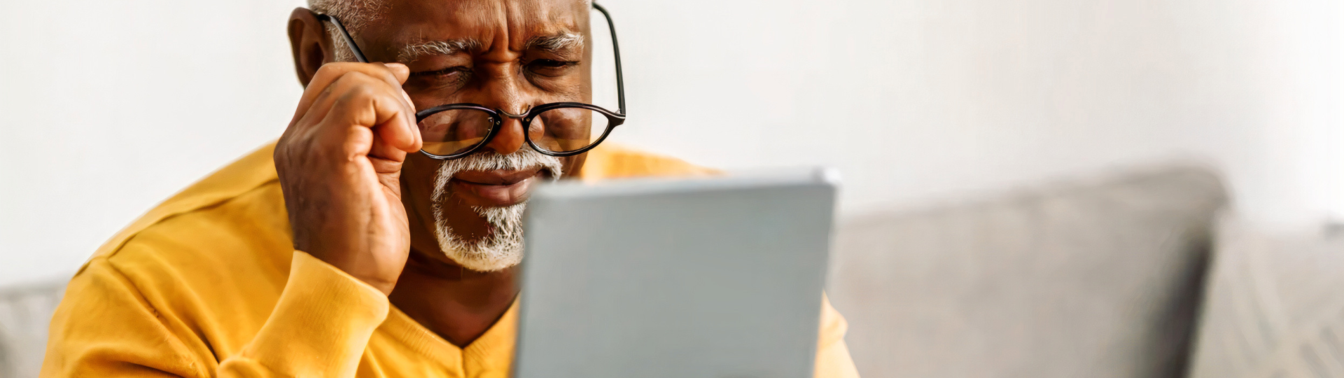 "Senior man wearing glasses and having difficulty viewing tablet, symbolizing the importance of maintaining good eye health as we age"
