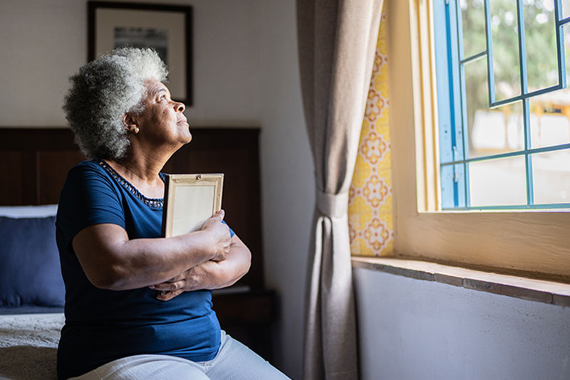 sad-senior-lady-holding-photo-looking-out-window-after-loss